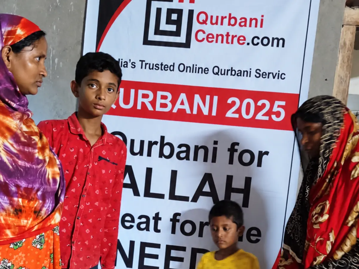 Two women and two children standing in front of a Qurbani Centre banner about Qurbani for Allah and meat for the needy